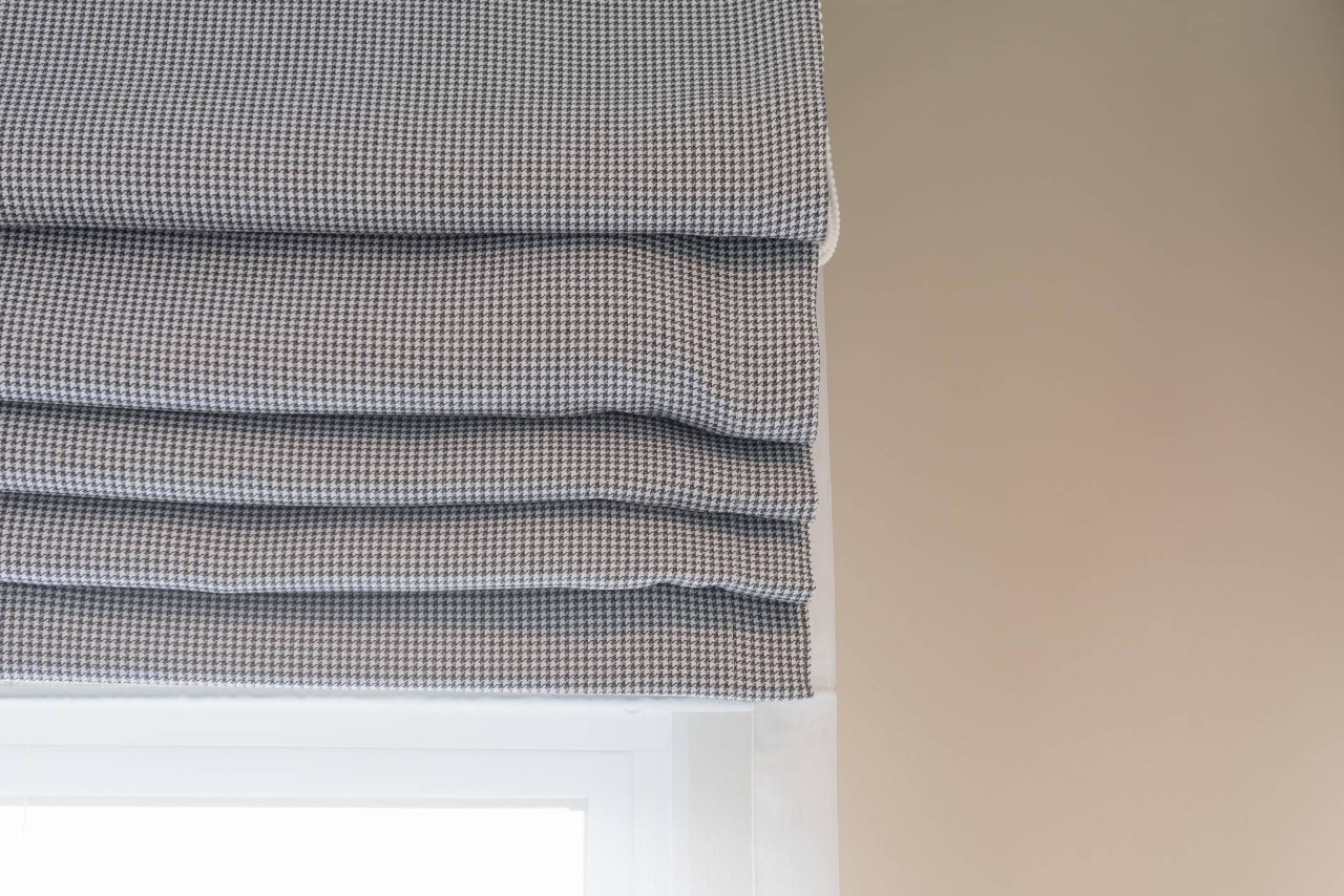 Upclose of small checkered patterned Roman shades on a window in a neutral color palette home at Blinds ‘N’ Shades Express near Campbell, CA